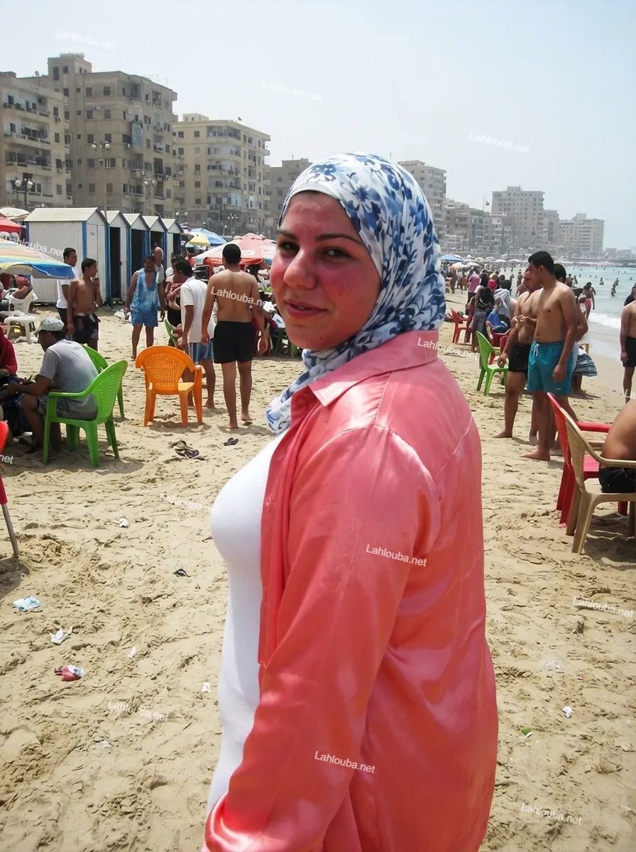 فتاة مصرية محجبة ترتدي قميصًا حريريًا ورديًا وتيشرت أبيض على شاطئ مزدحم