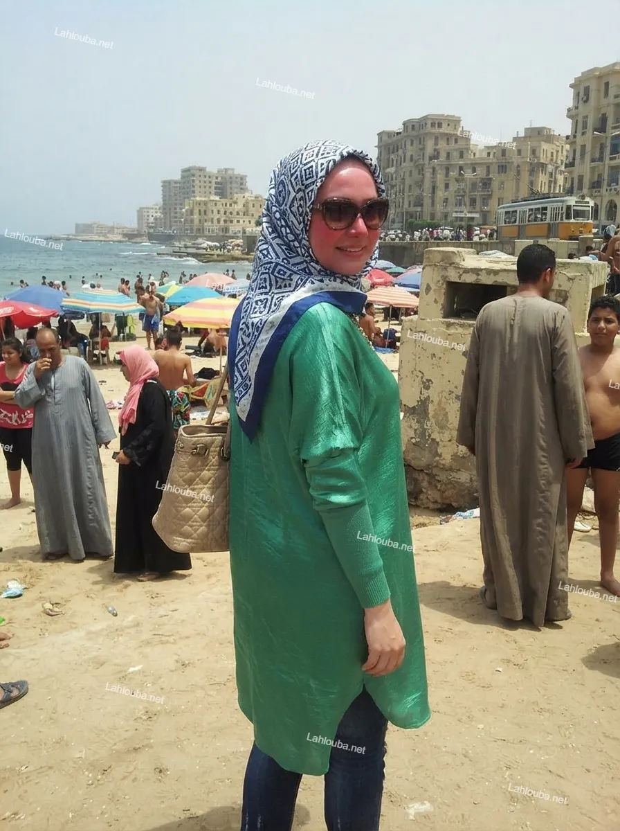امرأة محجبة ترتدي بلوزة خضراء وجينز على شاطئ مزدحم