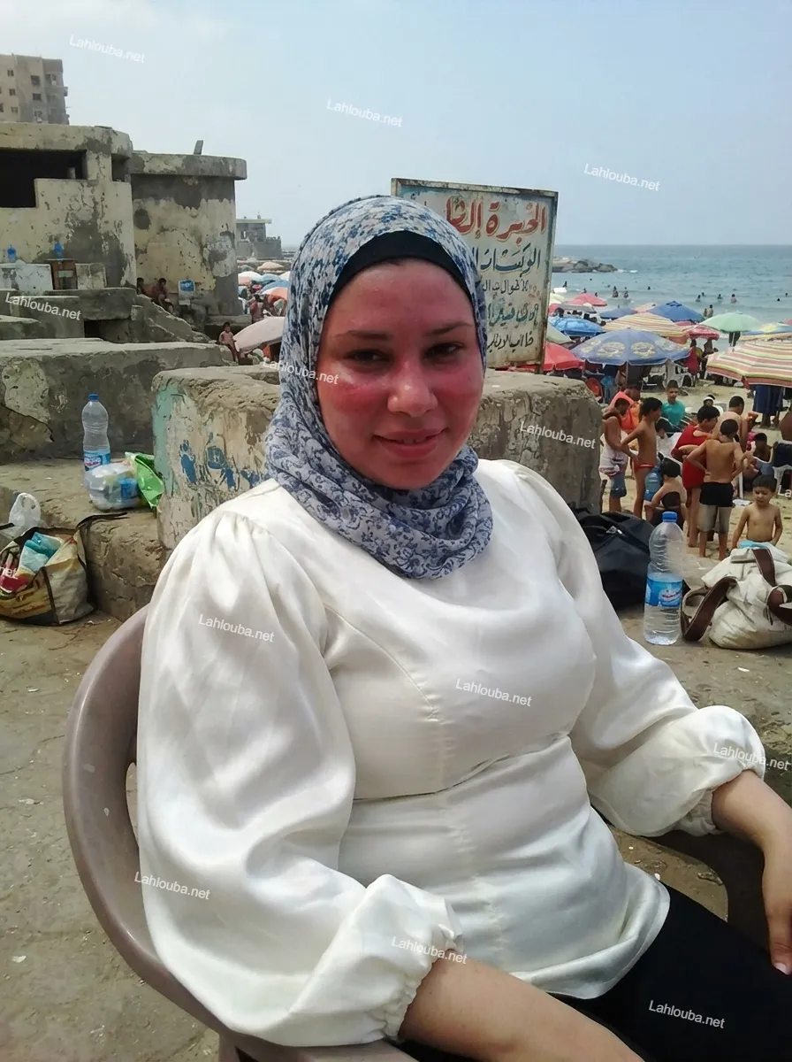 امرأة ترتدي حجاب أزرق وأبيض وبلوزة بيضاء حريرية لامعة على شاطئ شعبي