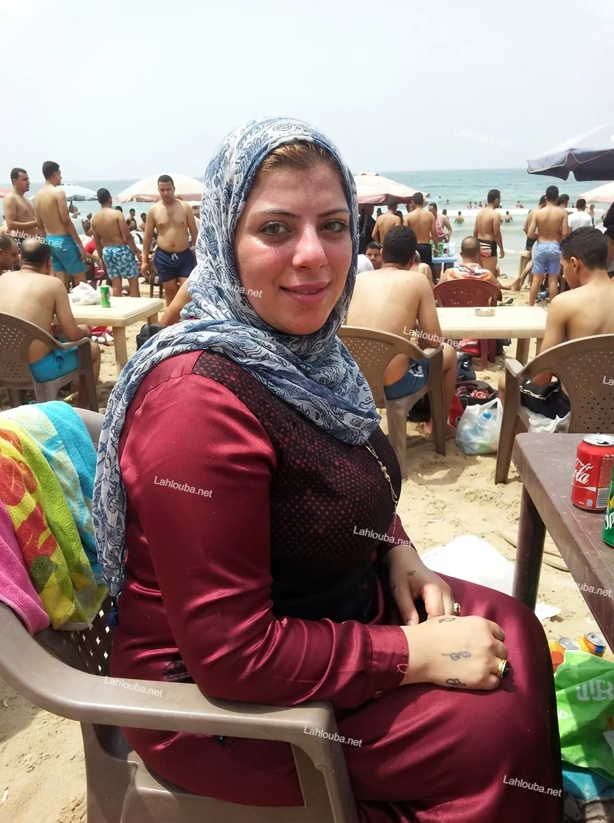 امرأة محجبة ترتدي زي بحر ساتر باللون العنابي وتجلس على الشاطئ