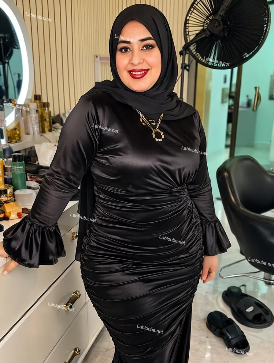 شابة ترتدي فستان أسود ساتان بأكمام مترفلة وتفاصيل كراويل مع طرحة حجاب سوداء