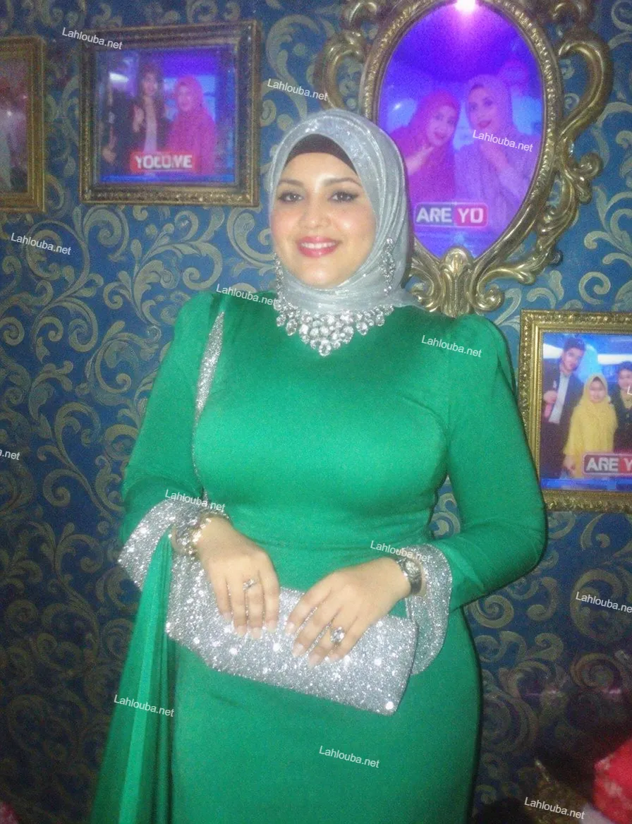 امرأة ترتدي فستان أخضر ساتان طويل الأكمام مع حجاب فضي مطرز وسلسلة بلورية كبيرة
